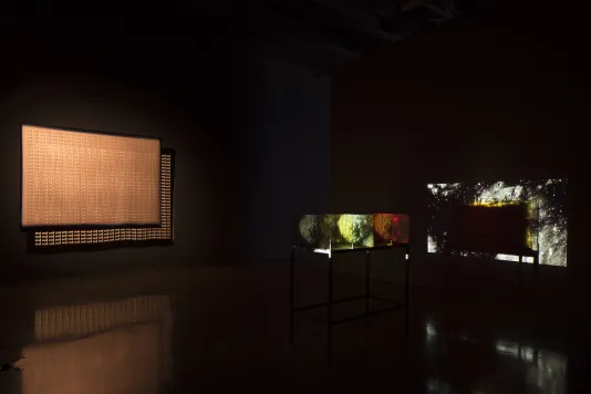 Lit orange screen hangs next to the colorful projection of planetary orbs through the glass panels of a table sculpture.