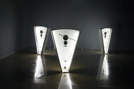 3 triangular sculptures, each internally-lit and fitted with 35mm film and spools, sit tilting in various directions.