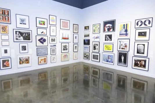 Corner of a gallery with small works of art hung salon style floor to ceiling. 