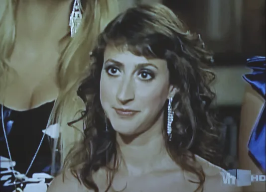 Close-up of the curled hair, made-up face and bare shoulders of a young woman wearing sparkly dangling earrings.