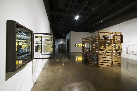 A large gallery with a slatted wood structure like a cabin, and a wall work with mirrored box and a glass window at an angle