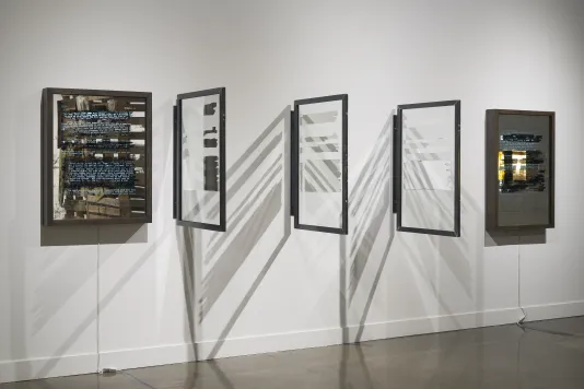 Five wall pieces in a row. Three in the middle with framed glass at 45 degree angles,  and a light box with text at each end