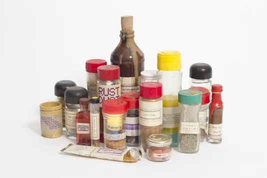 A group of labeled spice jars, different sizes and some with bright color lids, a flat tube, and a taller jar with a stopper