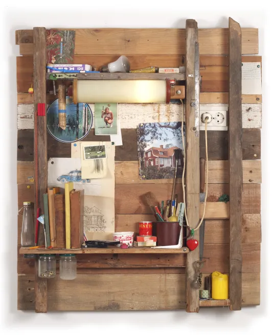 A slatted wood wall, shelves and objects like books, a light bulb, pictures, a tin with pens, an electric plug, a red heart