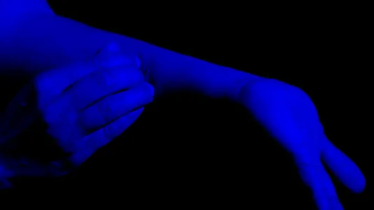 Blue colors the image of a right hand touching part of the left arm with flexed left hand against a black background.
