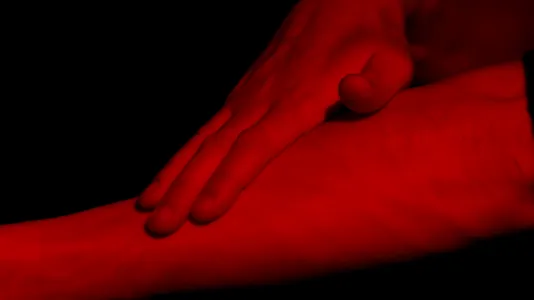 A hand on an arm is colored red against a black background.