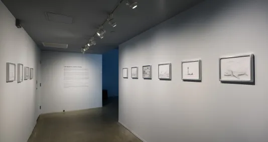 An entry space with framed drawings on left and right walls, wall text straight ahead, and the opening to another space