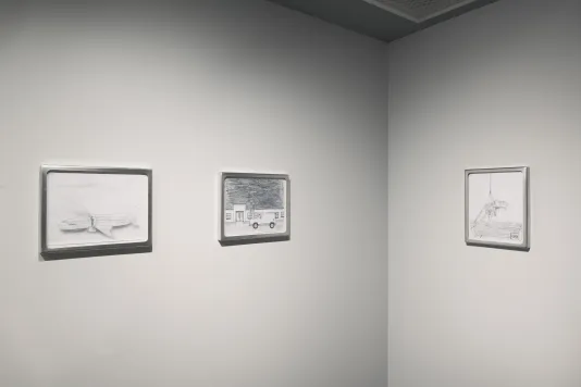 Installation view of a corner space with two framed graphite drawings on the left wall and one on the wall to the right