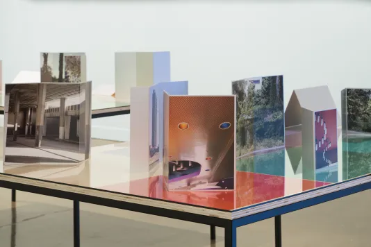 Installation view of table top with color gels under glass, various color photographs on aluminum placed at different angles