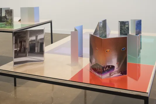 Installation view of table tops with color gels under glass, and with various photographs on aluminum folded at angles