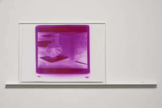 A saturated purple and white print behind glass on a white wall, a thin shelf running underneath