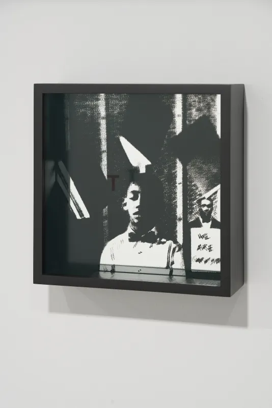 Shadowbox with a letter T on top glass over a silk screened image of a boy in the center, a man behind a sign to the right.