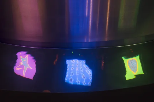Three brightly colored video images are reflected in the water of a curved stainless steel trough.