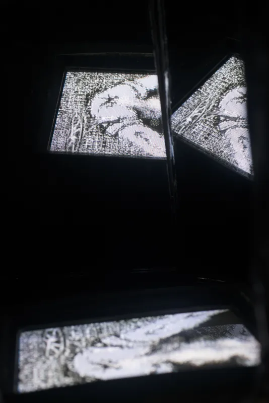 Three black and white screens appear to float within the dark space, displaying the same video image at different angles.