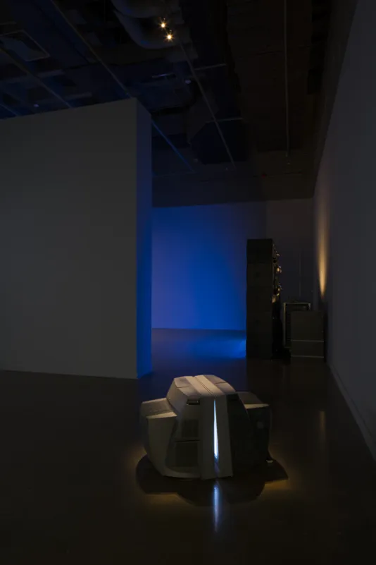Two monitors sit on the floor, screens pressed together, and a blue light emanates from a display in the room beyond.