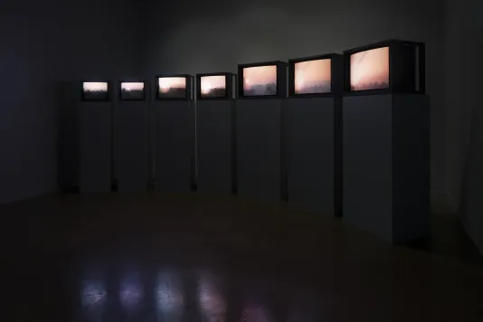 In a dark room, a curved formation of video monitors display a succession of sunrises.