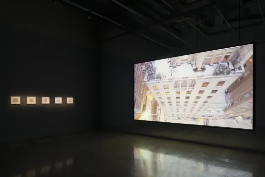 Dark room with a large screen showing a dizzying aerial view of a snow covered city high rise. 5 artworks hang to the left.