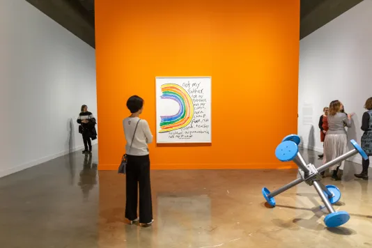 A visitor stands in front of an orange wall with an artwork that reads &quot;Not my father, not my brother'