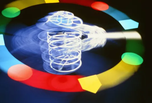 Video still of an almost complete circle comprised of different colors and shapes. In the center, imagery suggests a vortex.