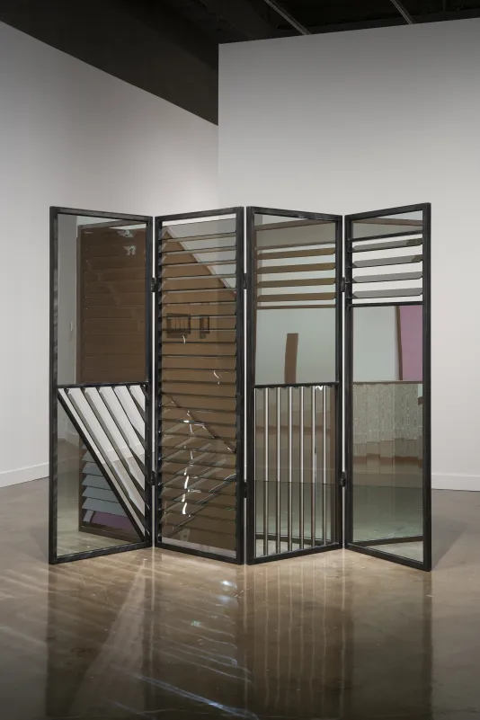 A mirrored, louvered privacy screen stands in the Gallery. Other artworks are visible through and reflected in this one.