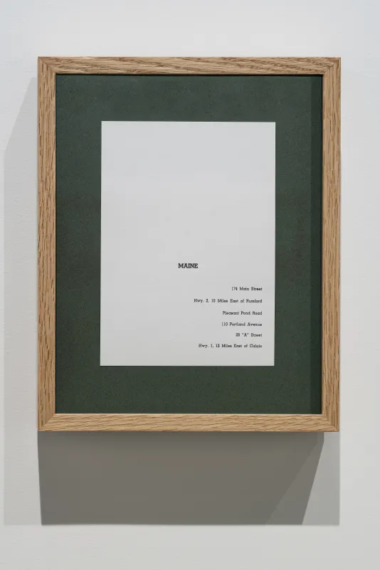 A vertical wooden frame with green matting and a piece of paper on which the name, Maine and 6 partial addresses are typed.