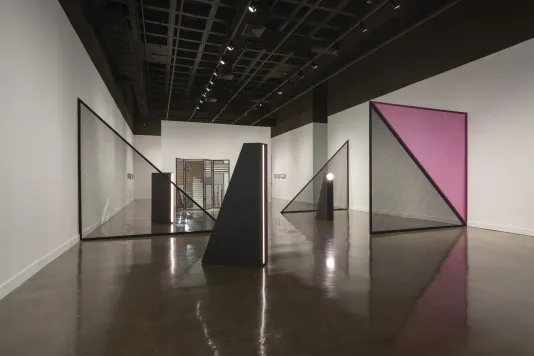 A juxtaposition of black triangular light sculptures, with large mesh black and pink triangles and a mirrored folding screen.