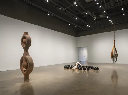 Three large artworks, including a part of a ship’s boiler, linked bowling balls and hanging metal strips surrounding beads.