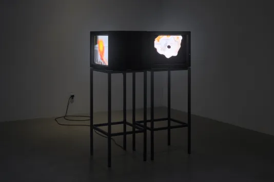 Two video monitors sit on metal stands placed adjacent and perpendicular to each other in a darkened room.