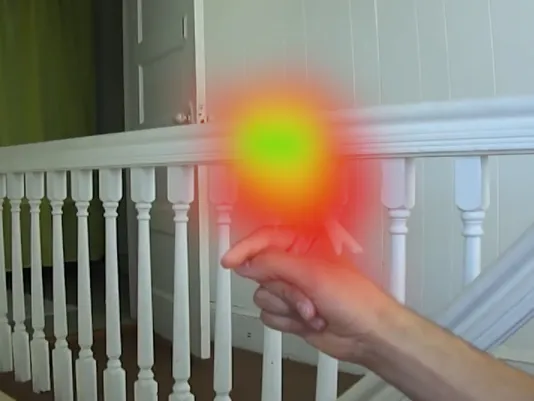 A hand and arm extended into an interior stairway with white railing and balustrades. A bright, flame-like, over-exposed object sits atop the hand.