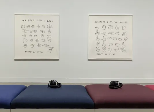 Close up of blue and red cushions and 2 headphones in front of 2 framed drawings of hands forming signs for the “ALPHABET”