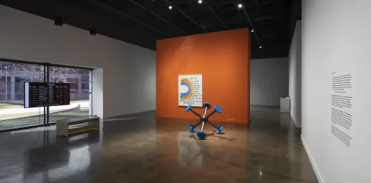 An orange wall divides the galleries featuring Sable Elyse Smith's "Coloring Book 33"