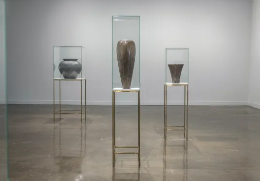 Three vases sit atop bronze pedestals inside a glass case.