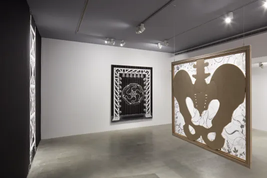 Installation view of hanging pelvic bone painting with black and white painting resembling a stage setup in the background. 