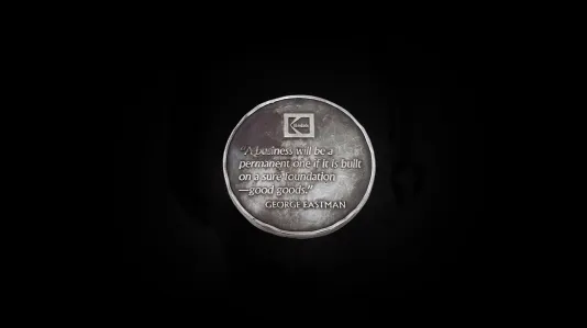 Patinated silver coin reads, “A business will be a permanent one if it is built on a sure foundation—good goods.” by George Eastman.