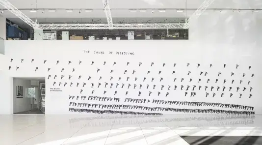 A mural by Christine Sun Kim features hand drawn letter &quot;P's&quot; on a white wall.