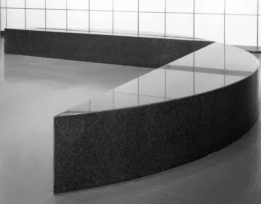 Black and white mage of a shiny, granite, semicircle shaped bench.