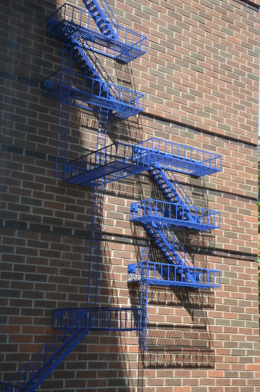 Brick wall with bright blue poles resembling a fire escape staircase.