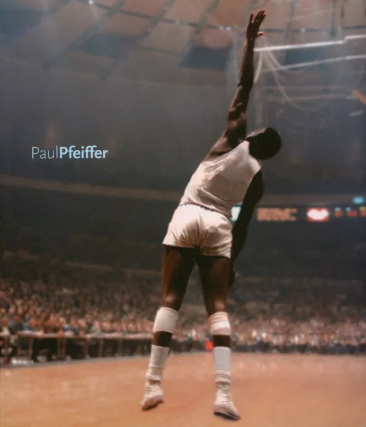 Book cover for Paul Pfeiffer featuring a manipulated photograph of a filled basketball arena and a single player, jumping with one hand up to block a shot