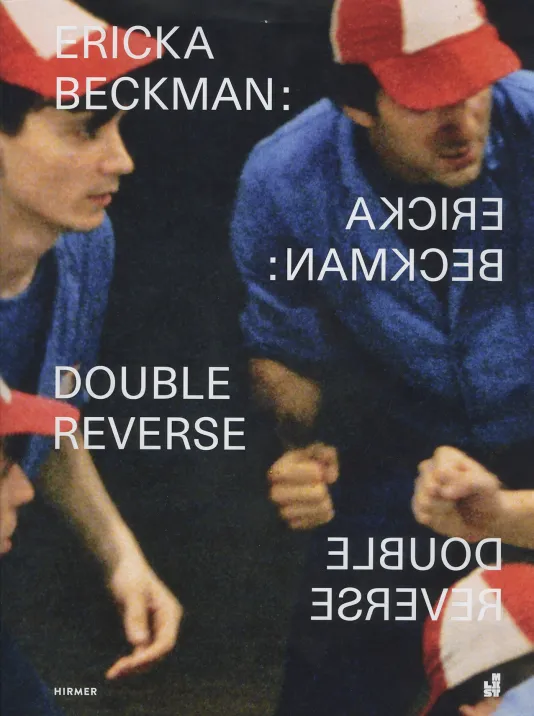 Book cover for Ericka Beckman: Double Reverse featuring a photograph of two men huddled in a circle wearing baseball caps. The exhibition title is shown reflected twice on the cover.