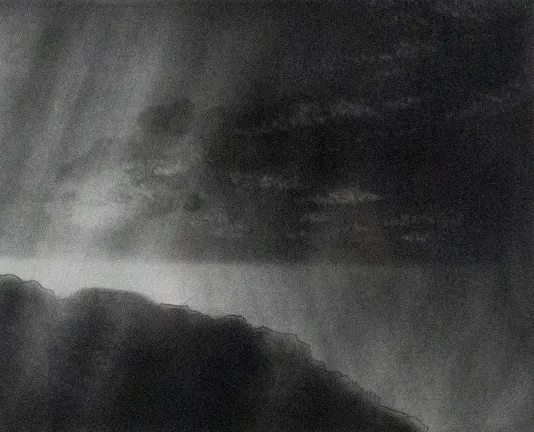 A dark misty sky with clouds above a rocky sloped hill silhouette.