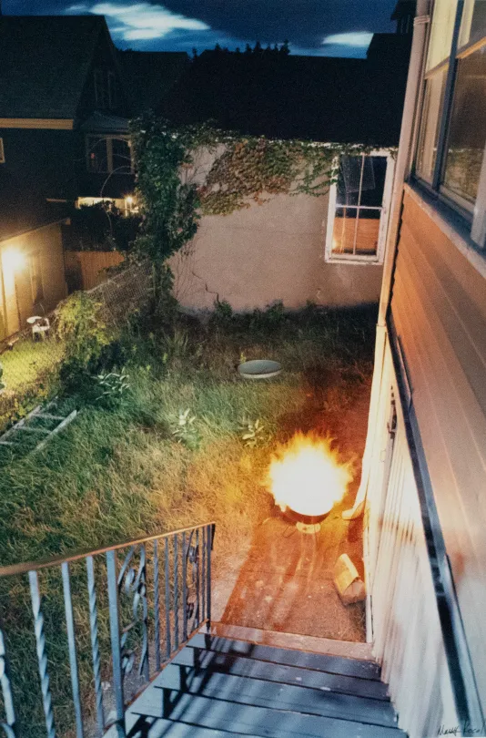 Photograph of a backyard from a staircase with a blazing fire in a small fire pit