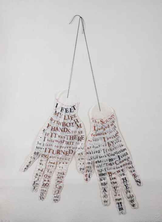 Pair of hands hanging fro ma string filled with letters and words cut out in different sizes.