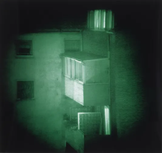 Nighttime photograph with a green hue of a porch that jets out of a building and a black vignette.