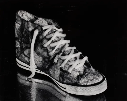 A dirty high top sneaker with a slight reflection below it and a black background.
