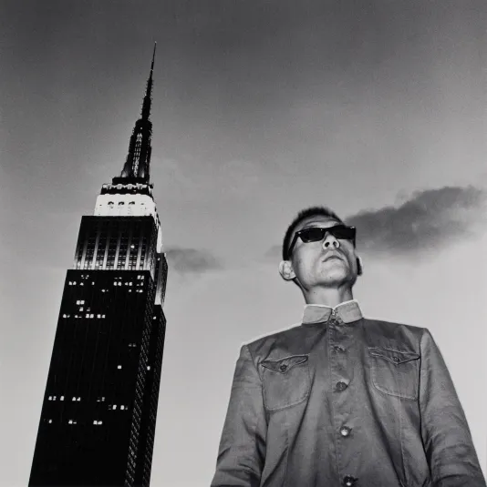 Black and white photograph taken at a low angle of a man wearing sunglasses with the Empire State Building to his left.