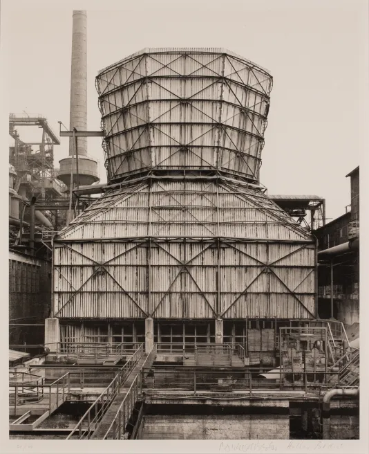 Black and white photograph of a wooden factory building with support beams on the outside.