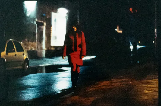 Night photograph of a person in all read walking down a dark sidewalk.