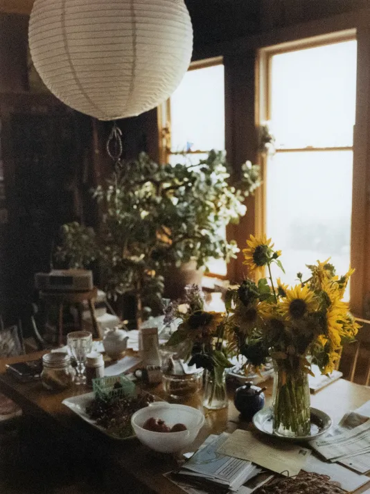 Photograph of a set dinner table with sunflowers in a vase on top and a round white lantern suspended above.
