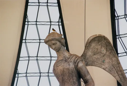 Photograph of a statue of an angel in front of a triangular glass wall.