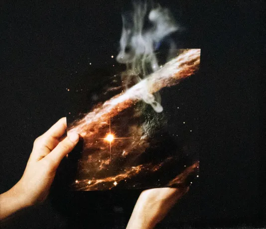 Photograph of someone's hands holding a photo of the galaxy with smoke rising at the top.